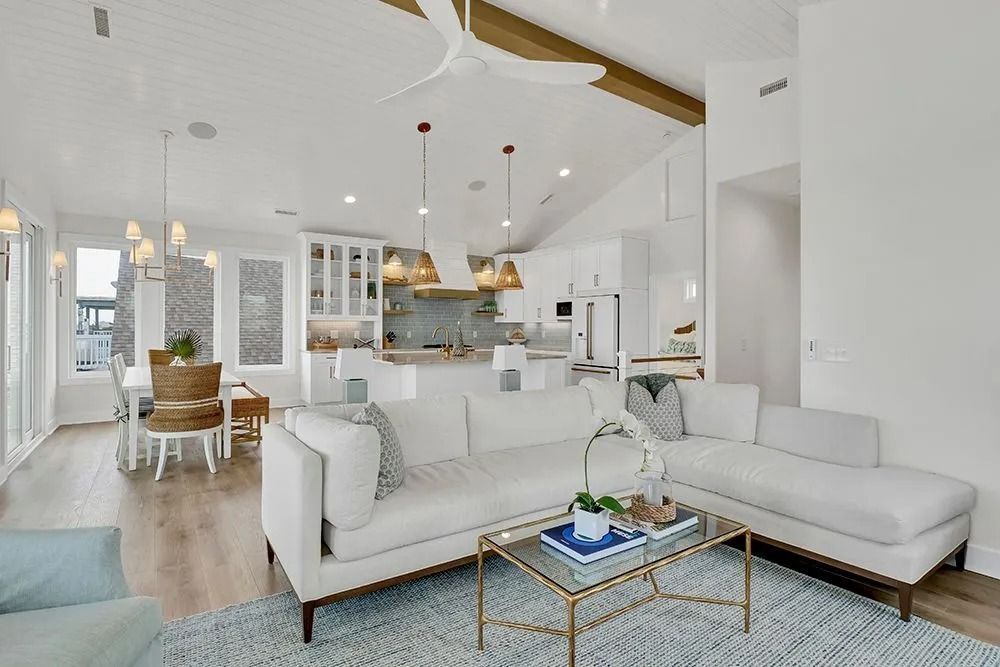 Spacious white living room with light wood floors, a sectional sofa, and a glass coffee table.