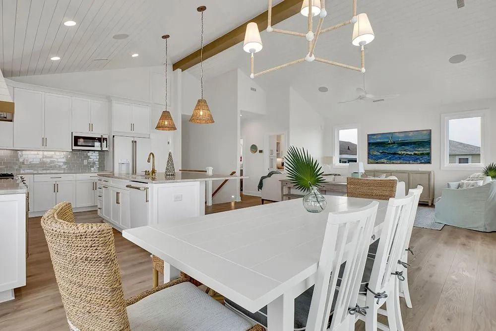Bright, open kitchen and dining area with white cabinets, table, and accents, with wood flooring and light fixtures.