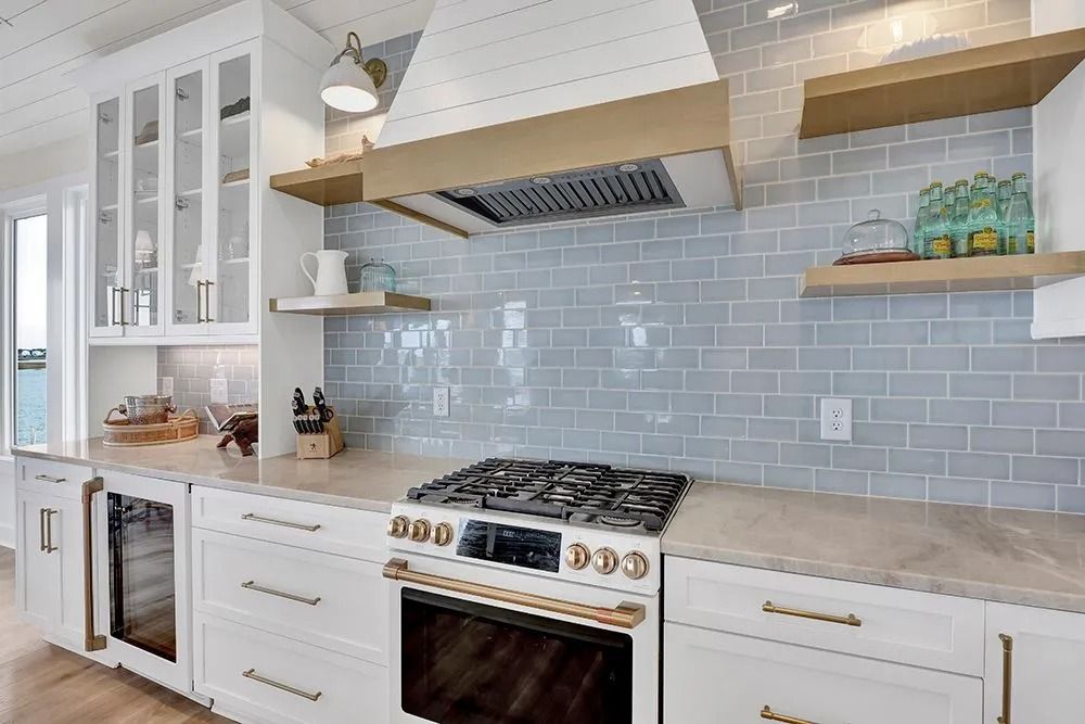 Coastal kitchen with blue tile backsplash, white cabinets, gold accents, and a range.