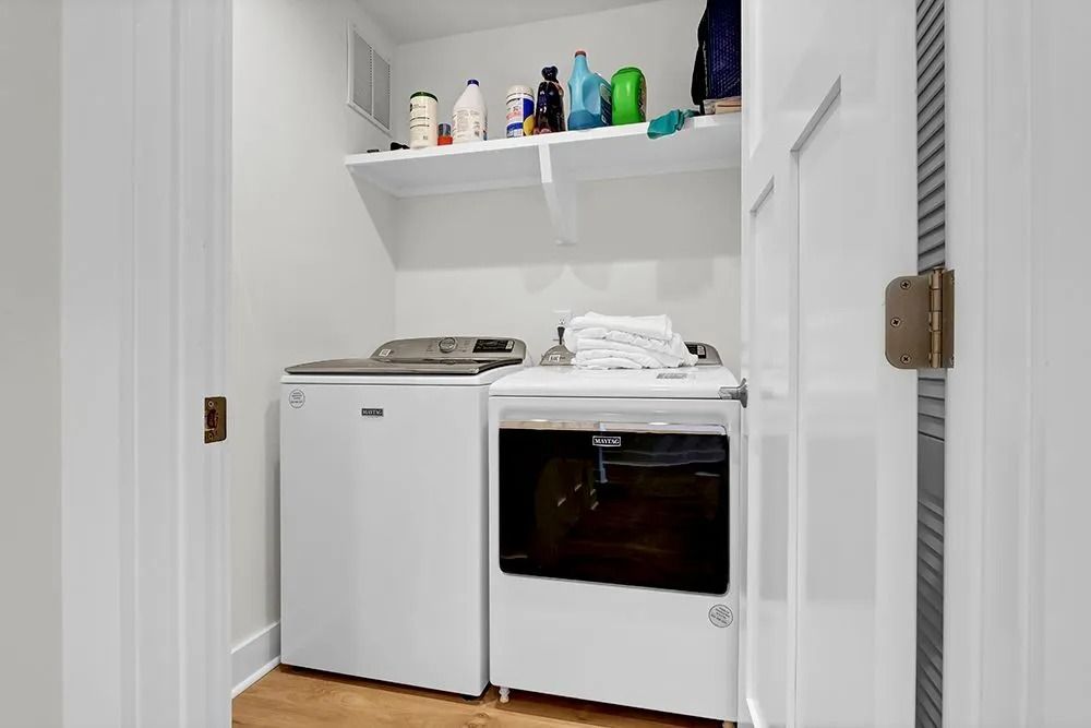 Laundry room with white washer and dryer, shelf with cleaning supplies.