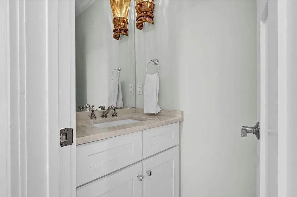 A small white bathroom with a sink, mirror, and two gold sconces.