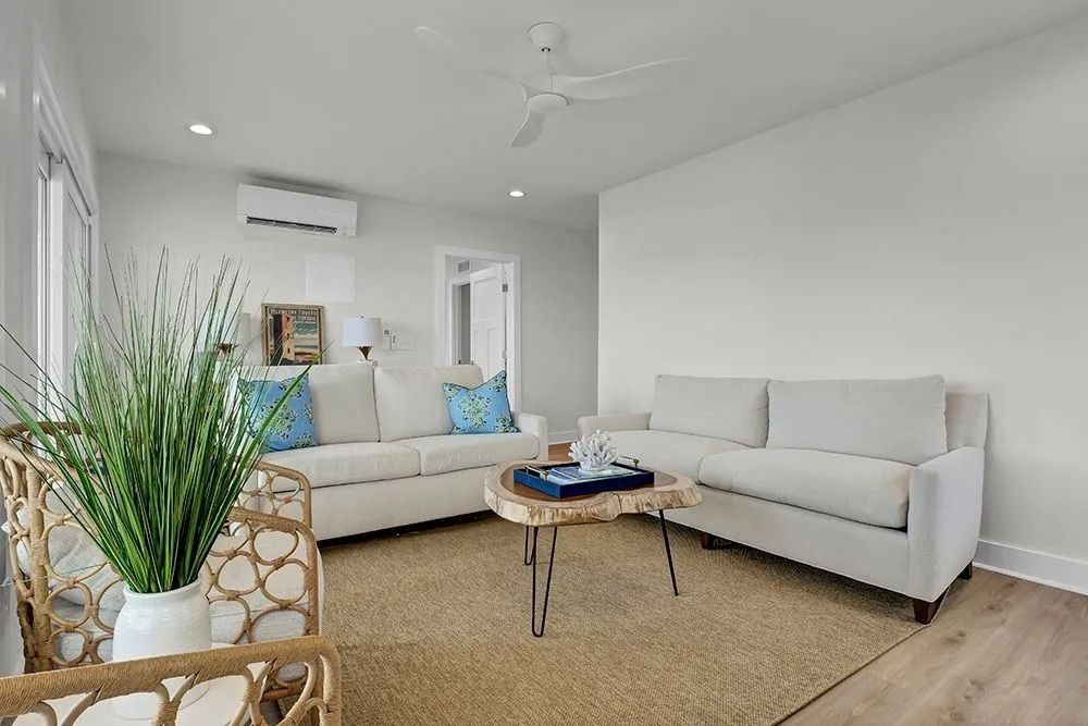 Living room with white sofas, jute rug, wooden coffee table, and air conditioning unit.