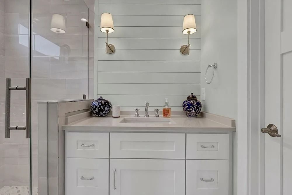 White bathroom with a white vanity, shiplap wall, sconce lights, and shower.