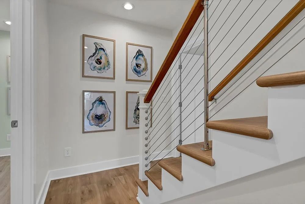 Staircase with wooden steps and railing, cable railing, and four framed oyster shell art prints on white wall.