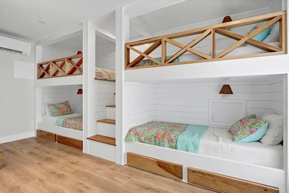 White bunk beds with wooden accents and drawers, in a bright, wood-floored room.