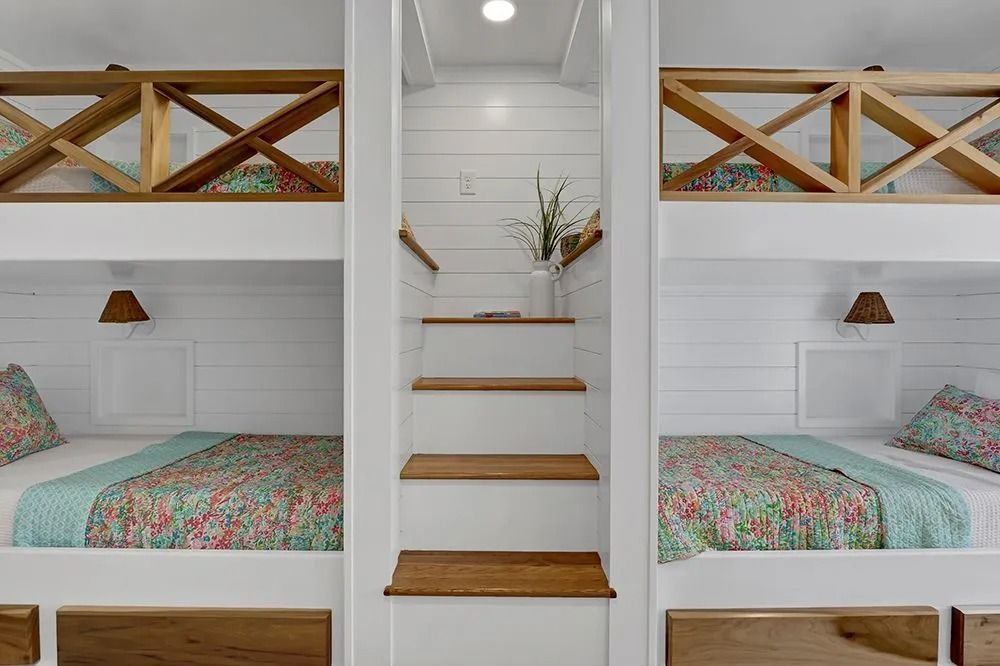 Built-in bunk beds with white paneling and wooden accents. Beds have floral quilts, stairs in the middle.