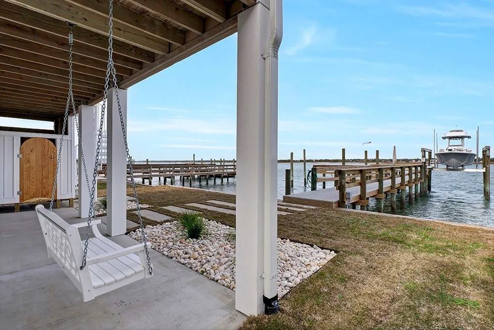 White porch swing overlooking a dock and boat, under a coastal home.