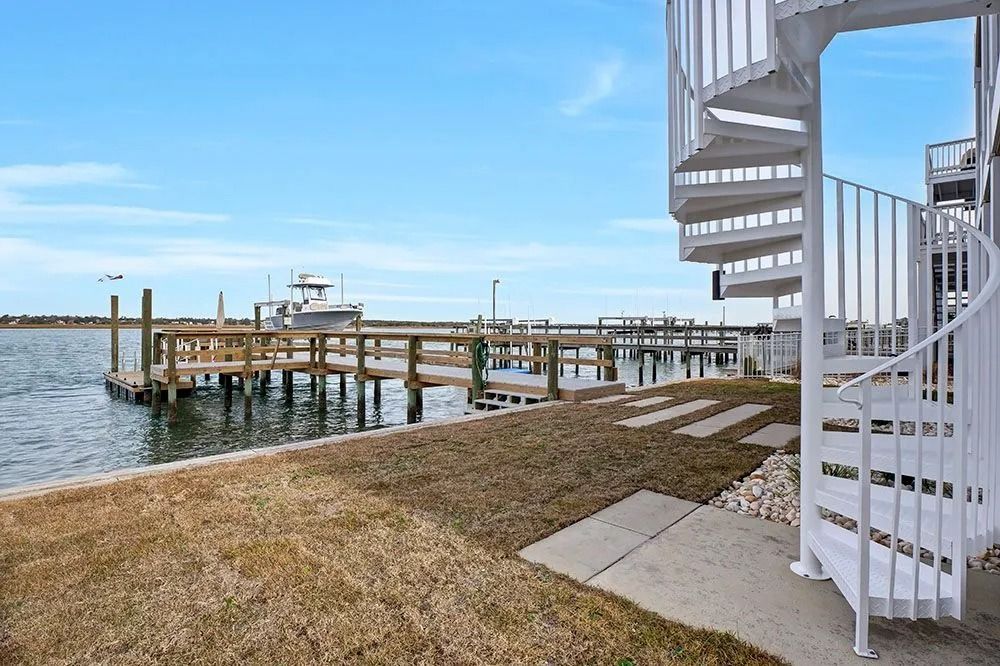 White spiral staircase next to a dock and water, clear blue sky overhead.
