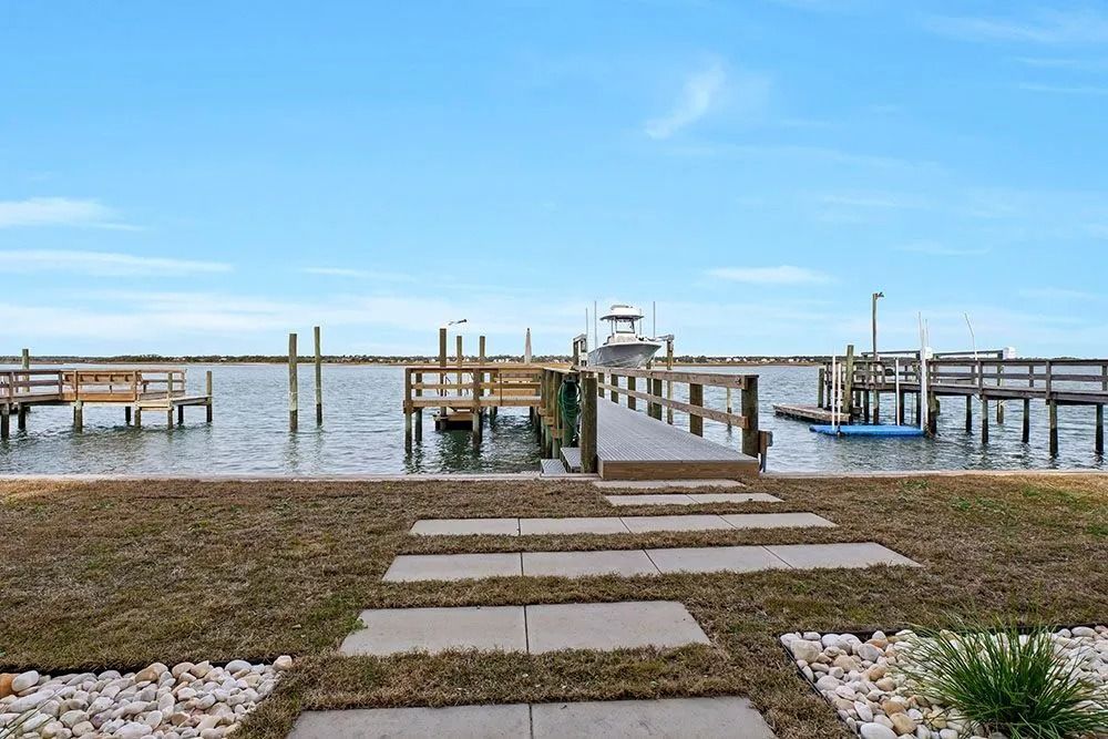 Docks on calm water under a blue sky. A pathway leads from grass to a wooden pier with a boat.