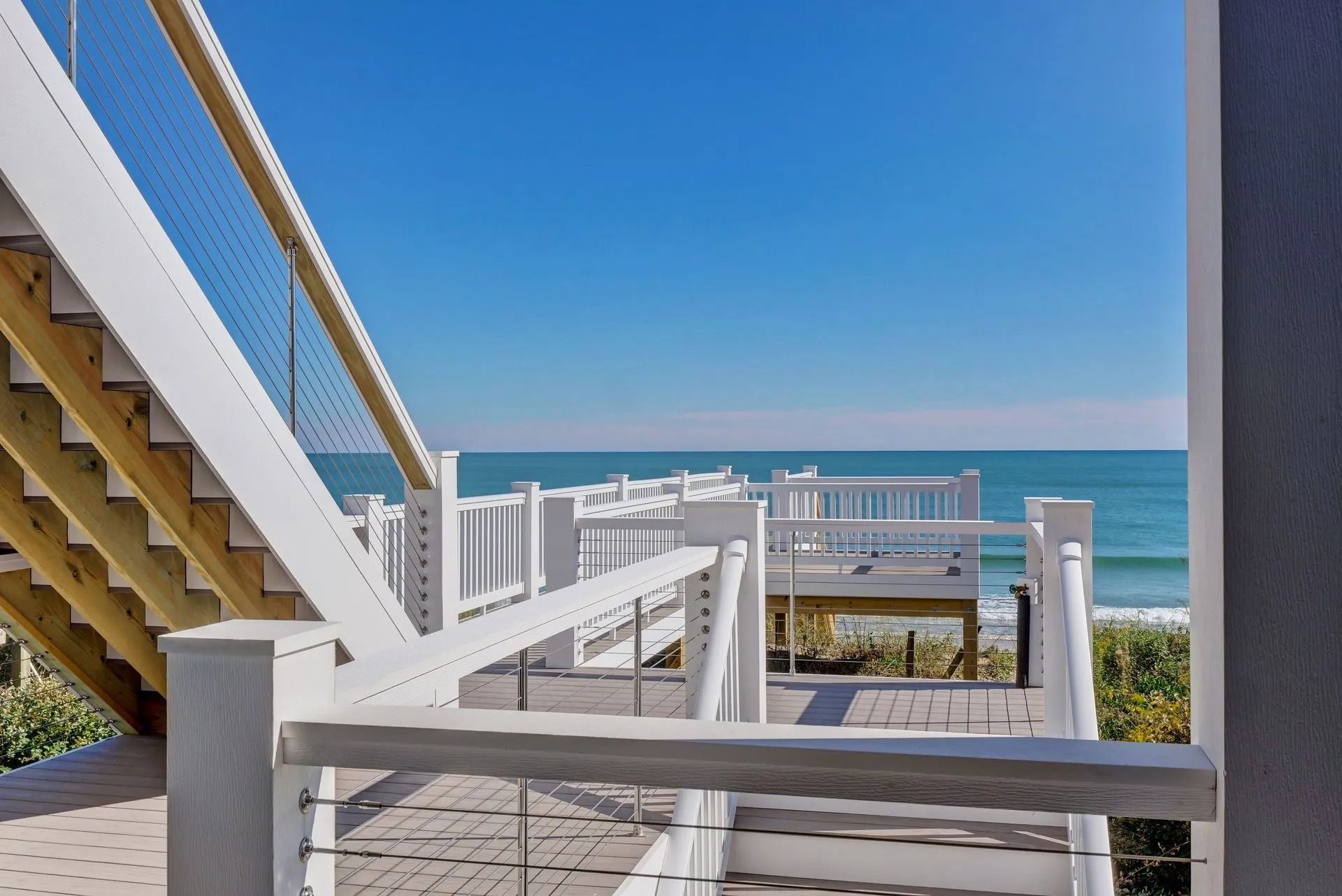 White stairs and deck overlooking a blue ocean under a clear sky.