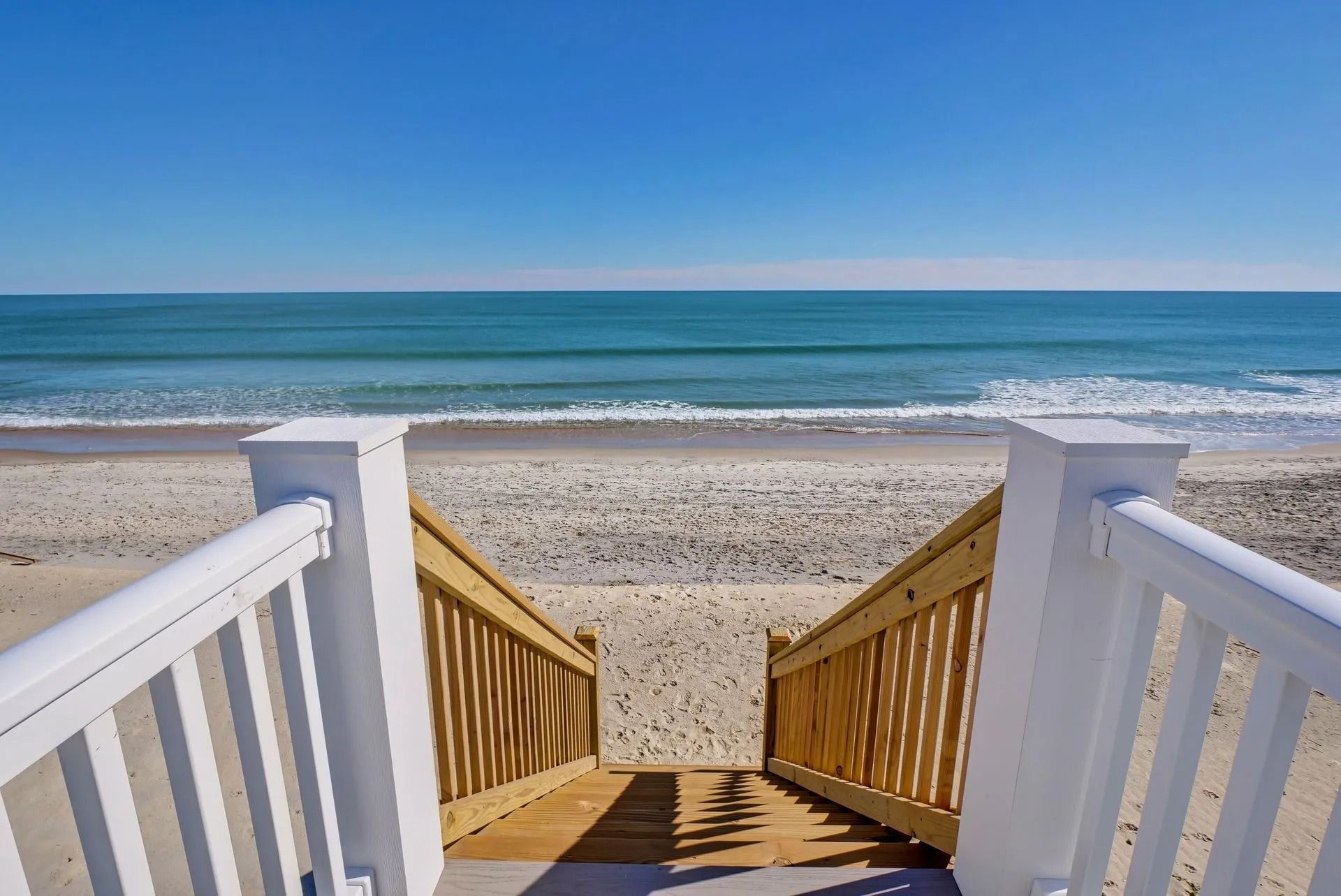 Wooden stairs leading down to a sandy beach and ocean under a blue sky.