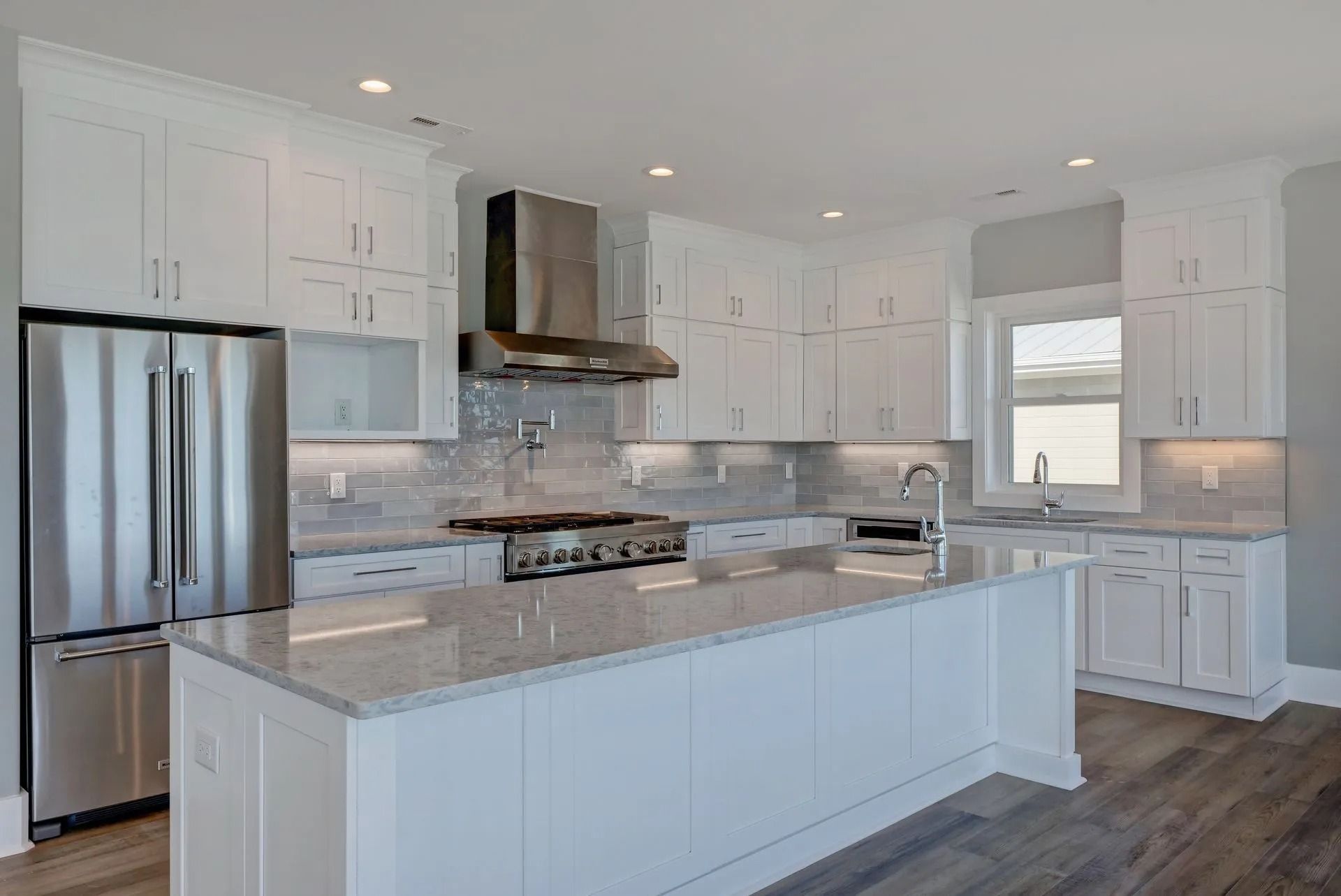 Modern white kitchen with stainless steel appliances, island, and granite countertops.