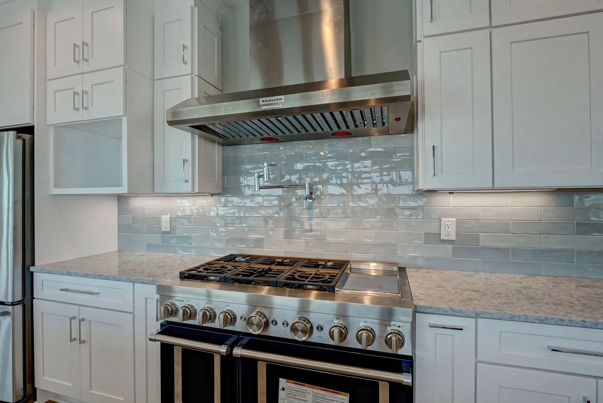 Kitchen with white cabinets, stainless steel appliances, and gray backsplash.
