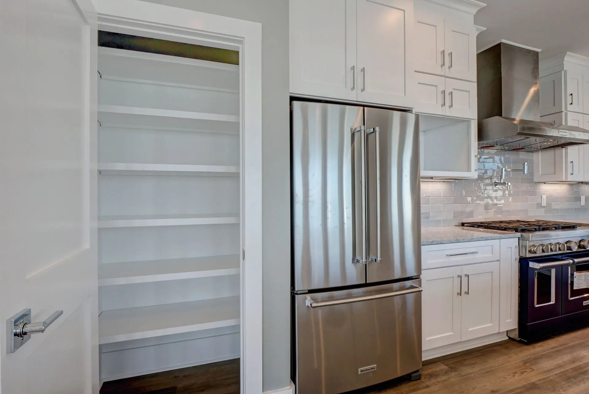 Kitchen with empty pantry, stainless steel fridge, white cabinets, and gas range.