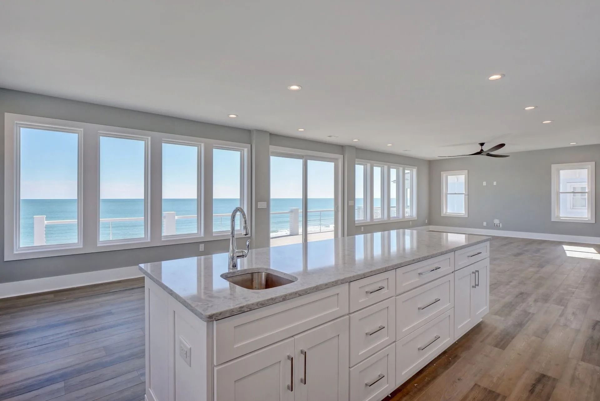 Bright kitchen with white island, sink, and ocean view through large windows.