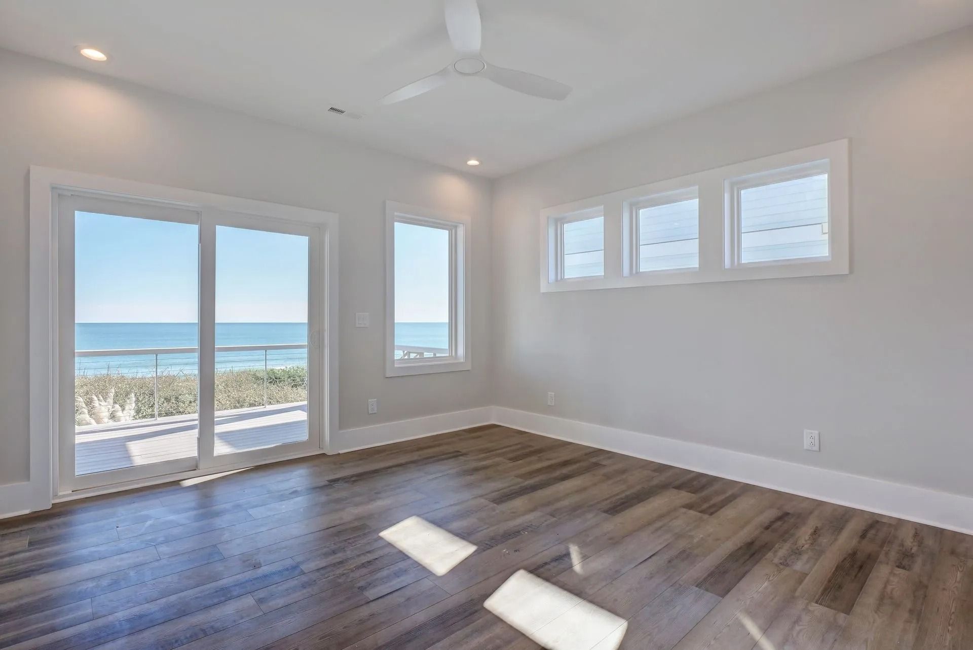 Bright bedroom with ocean view, sliding door, windows, wood floor, white walls.