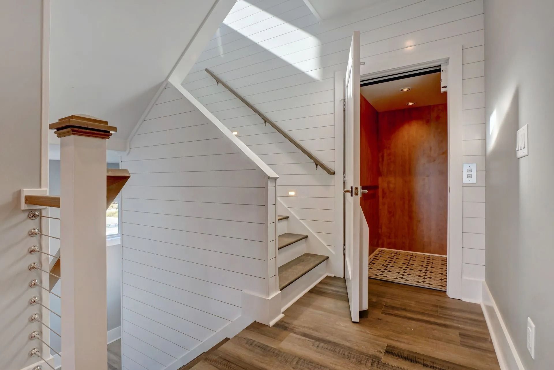 Staircase with white paneled walls, wood floors, and an elevator.
