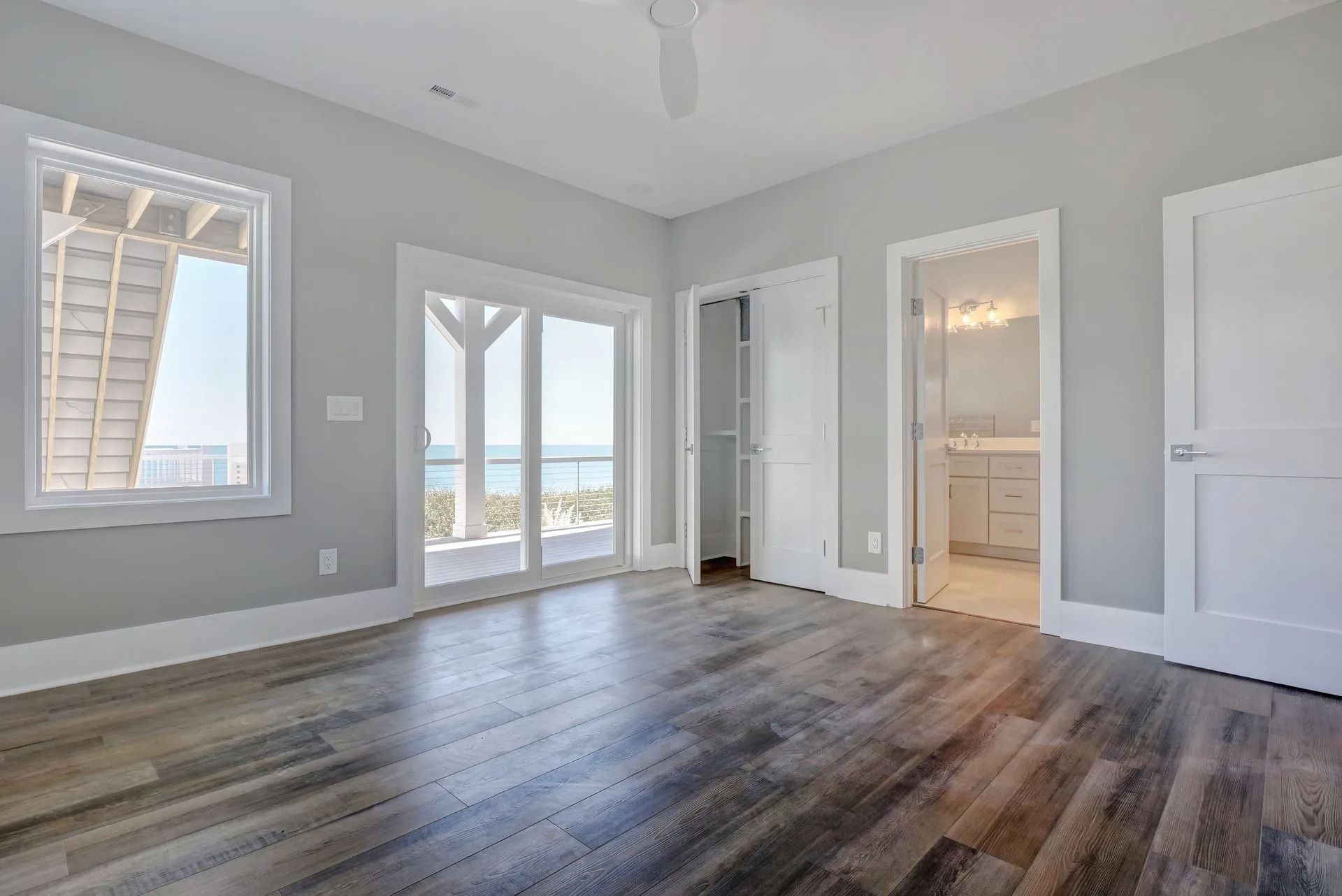 Bedroom with wood-look floor, gray walls, white trim, and a sliding glass door with a view of the ocean.