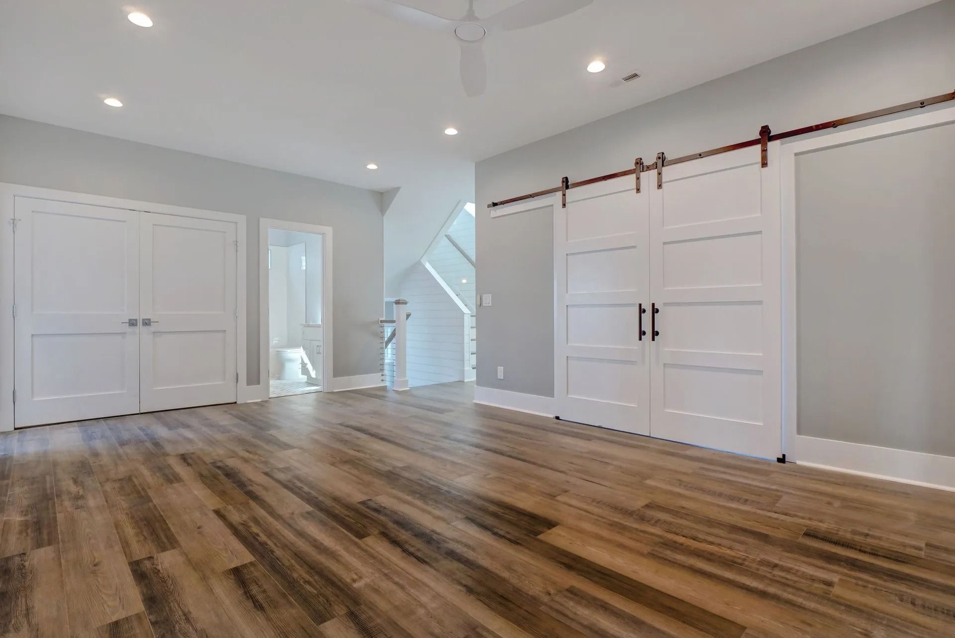 Empty bedroom with wood-look floor, white walls, two closets, and sliding barn doors.