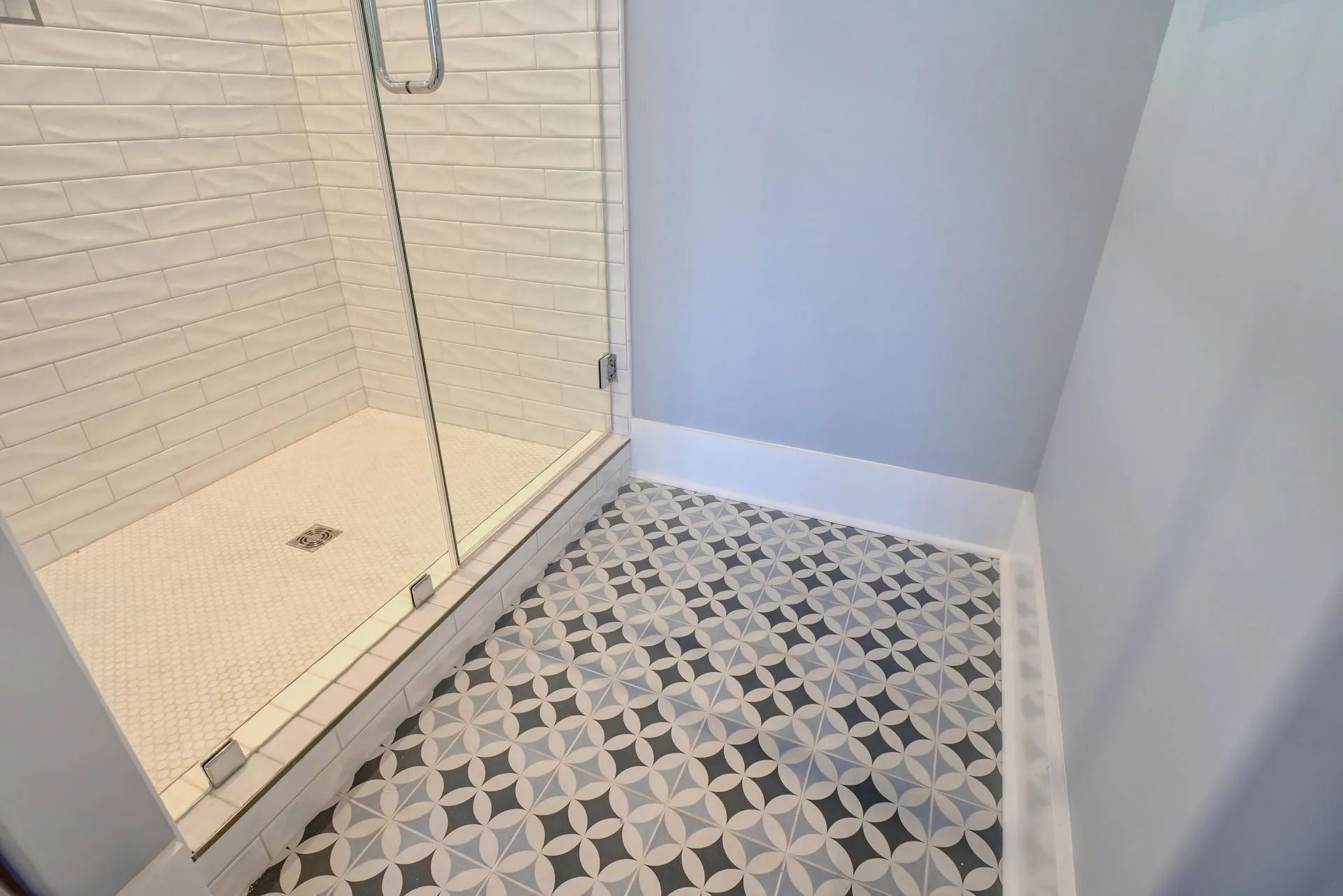 Bathroom with glass-door shower, white tiled walls, patterned floor tiles, and gray walls.