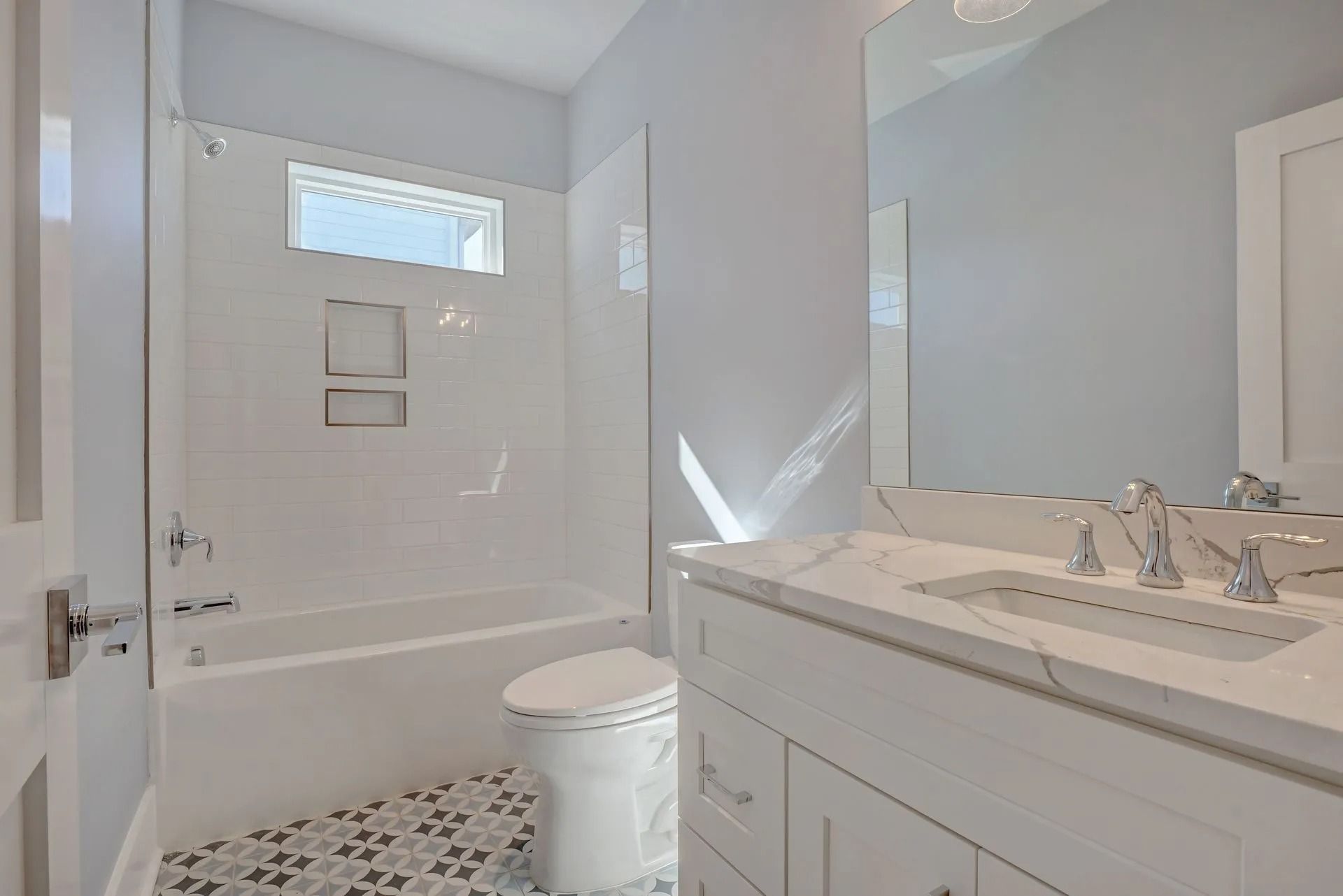 White bathroom with bathtub, toilet, and vanity; gray walls, patterned floor tile.
