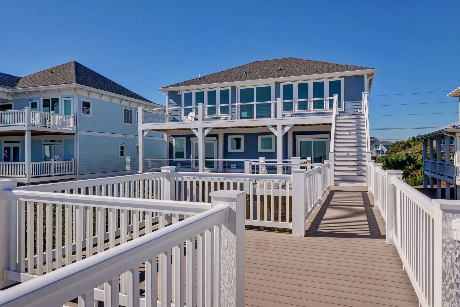 Blue beach house with white railings, a walkway, and a bright blue sky.