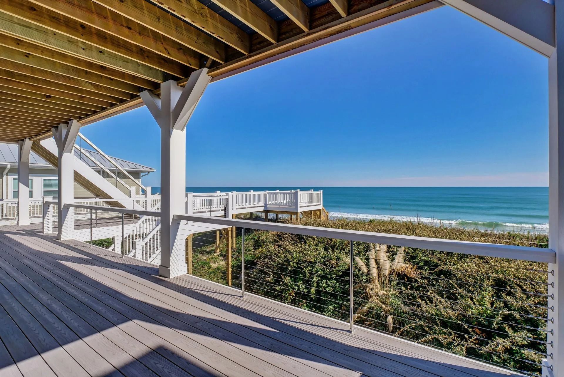Wooden deck overlooking the ocean. White railings and structure, blue sky, and waves.