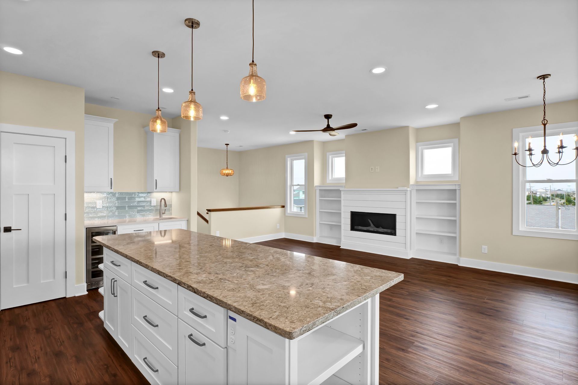 Spacious kitchen with island, white cabinets, and dark wood floors, open to a living area with a fireplace.