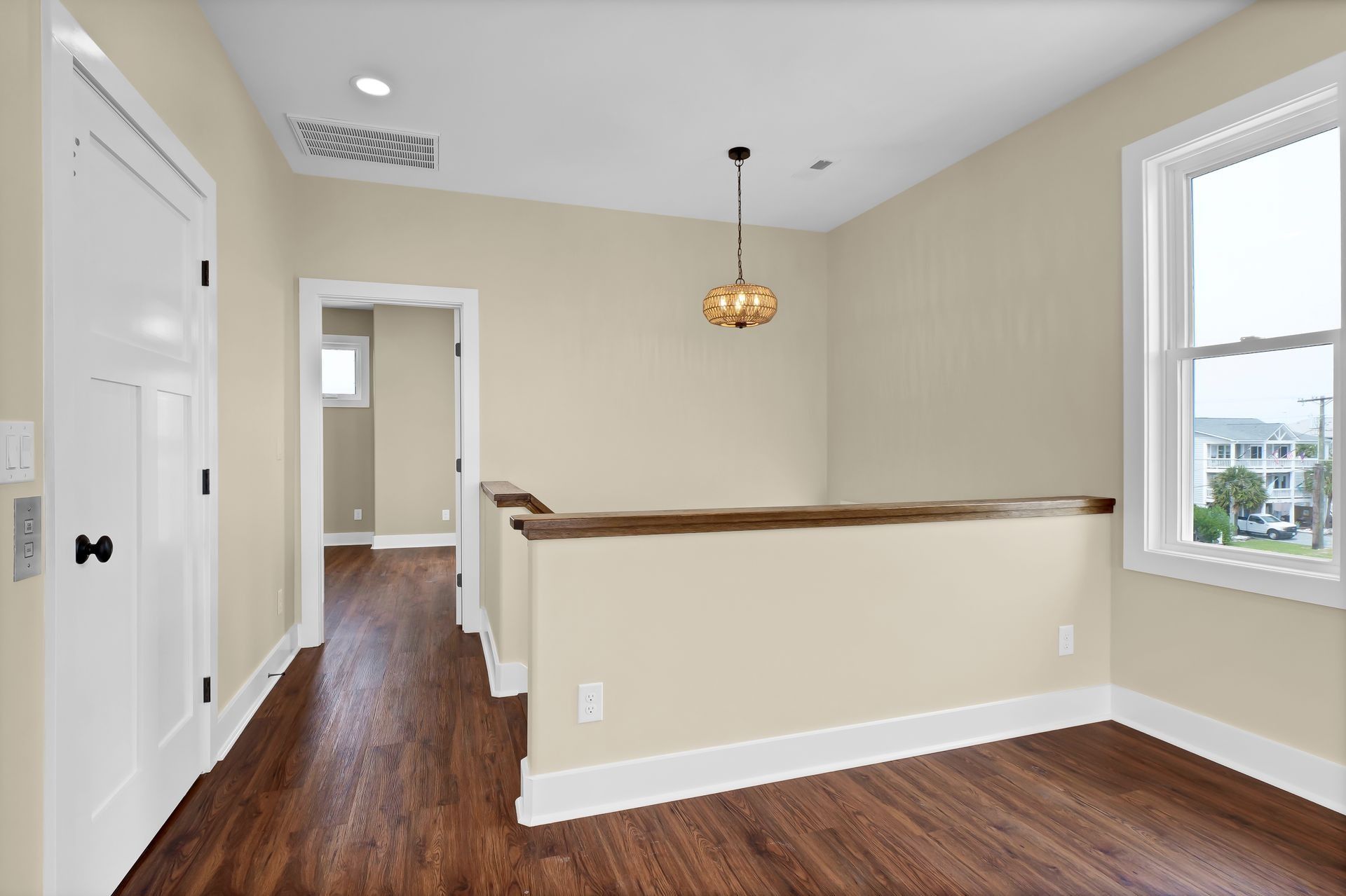 Interior shot of a hallway with hardwood floors, a door, a window, and a hanging light fixture.