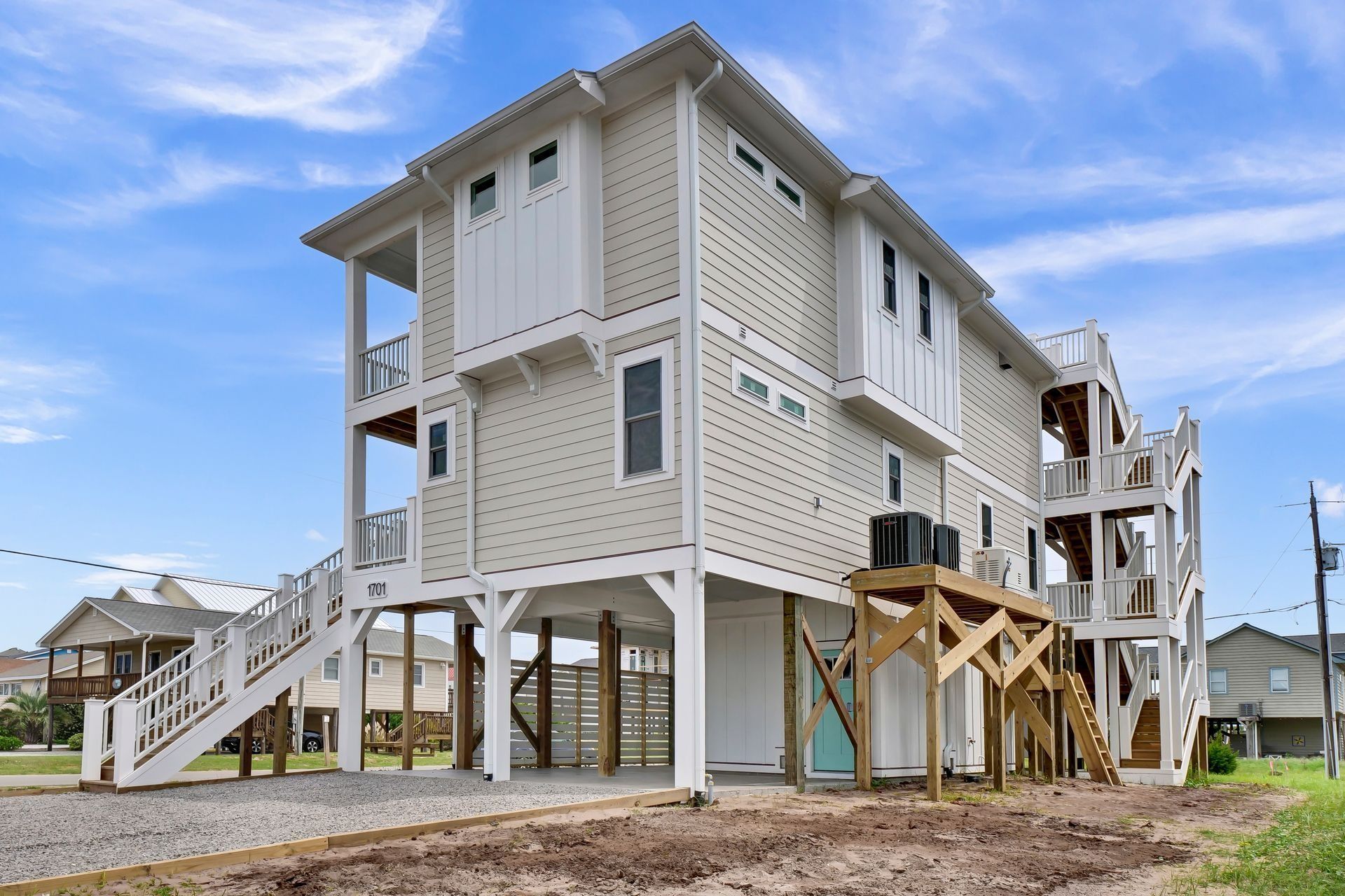 Multi-story beige and white beach house on stilts with multiple balconies, under a blue sky.