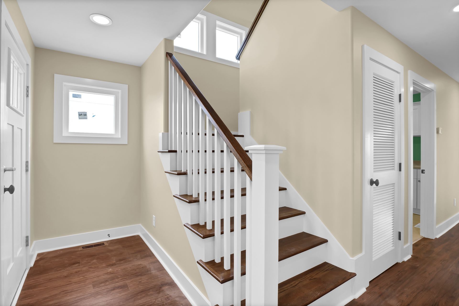 Staircase in a home with wooden steps and white balusters. Two doors and a window are visible.