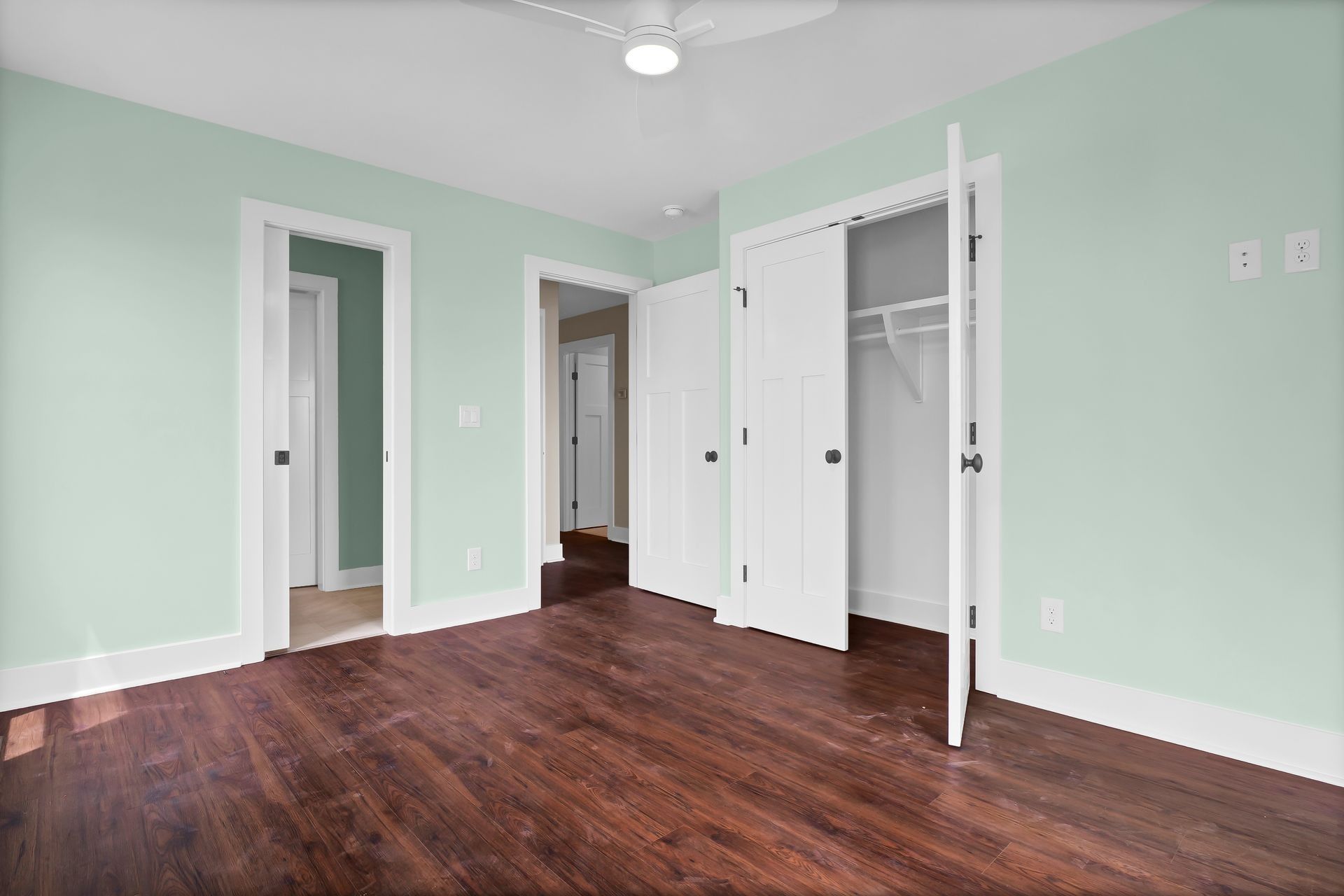 Empty bedroom with mint green walls, hardwood floors, and white trim. Closet doors are open.