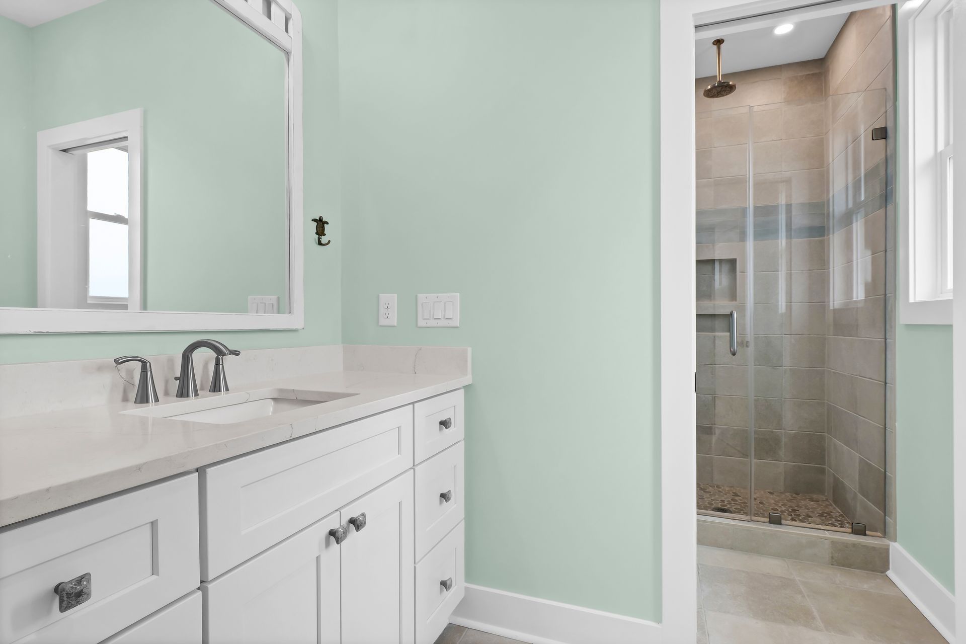 Bathroom with white cabinets, light green walls, a white countertop, and a walk-in shower.