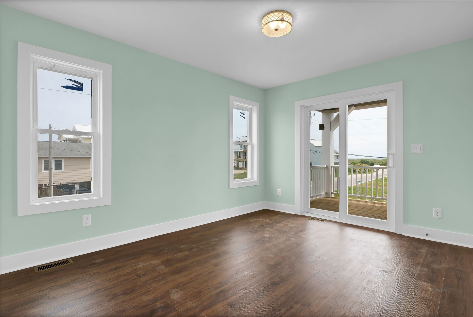 Empty room with pale green walls, brown hardwood floor, and a sliding door leading to a balcony.