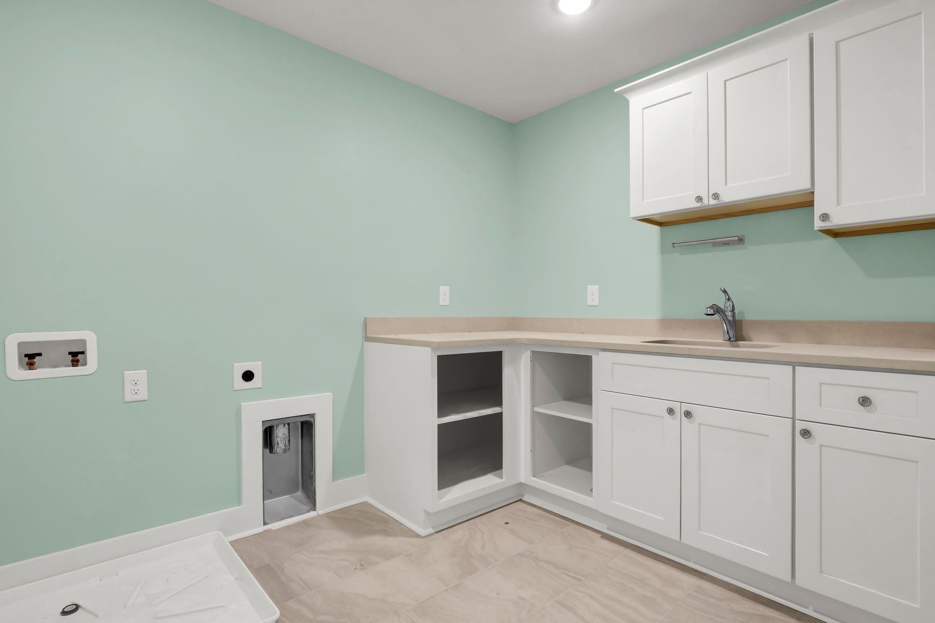 Laundry room with white cabinets, light countertop, pale green walls, and a sink.
