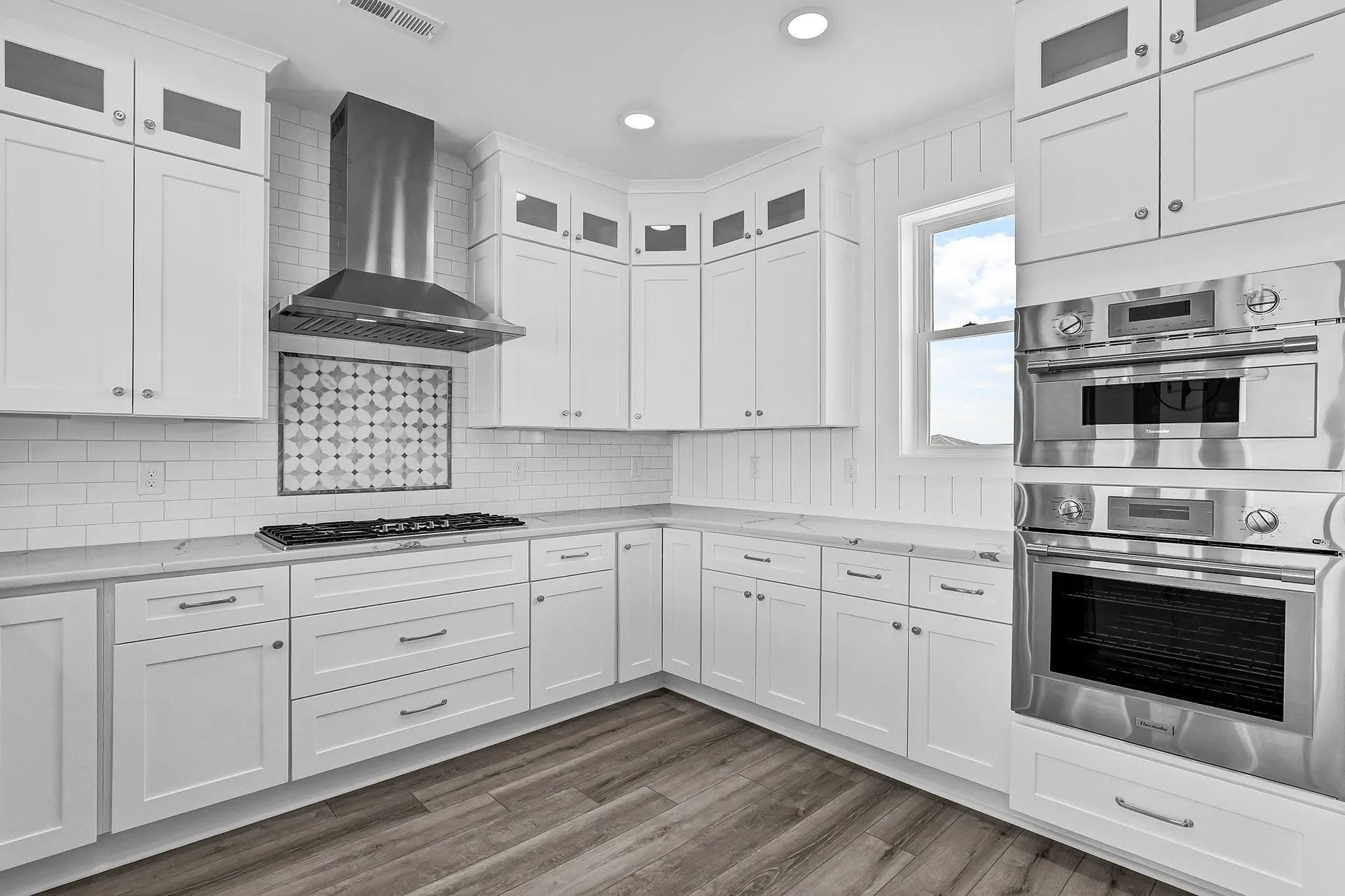 White kitchen with cabinets, stainless steel appliances, and wooden flooring.