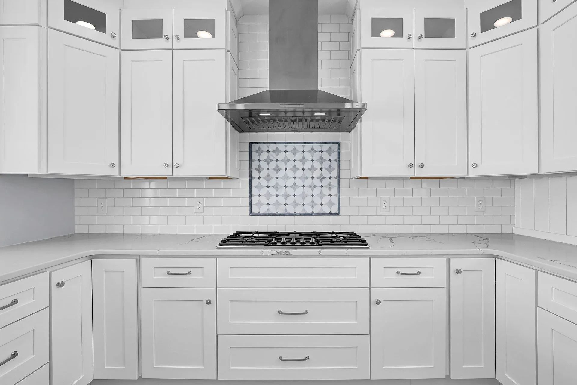 White kitchen with cabinets, stove, range hood, and tile backsplash.