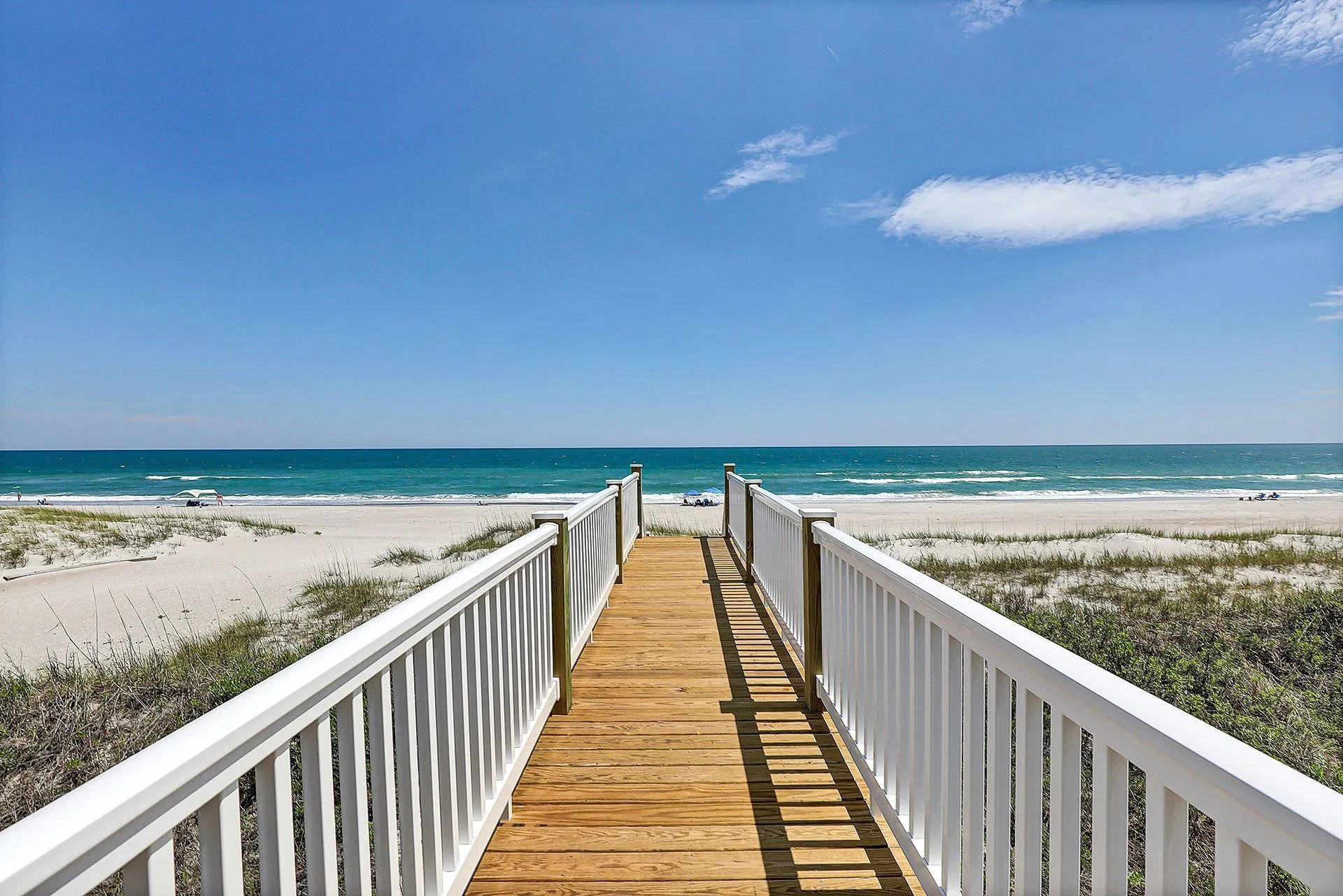 Wooden boardwalk leading to a beach with white sand, turquoise water, and a blue sky.