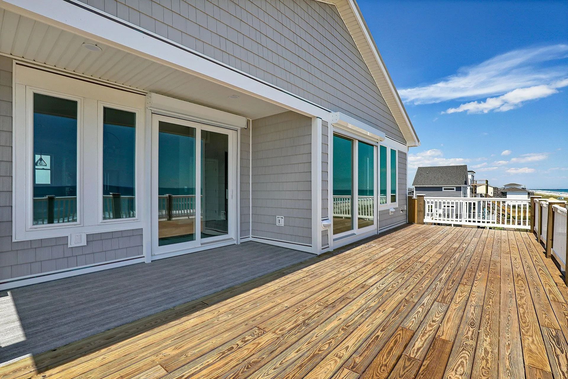 Wooden deck of a gray beach house with ocean view and blue sky.