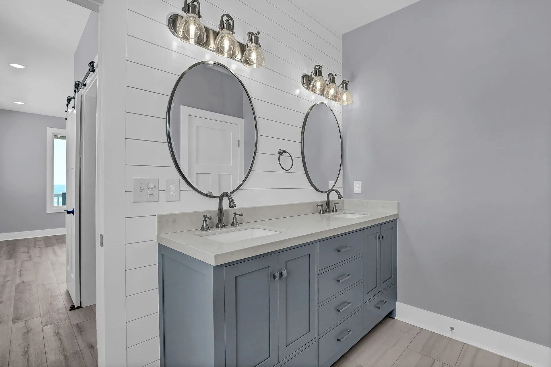 Bathroom with dual sinks, oval mirrors, blue vanity, and white shiplap accent wall.