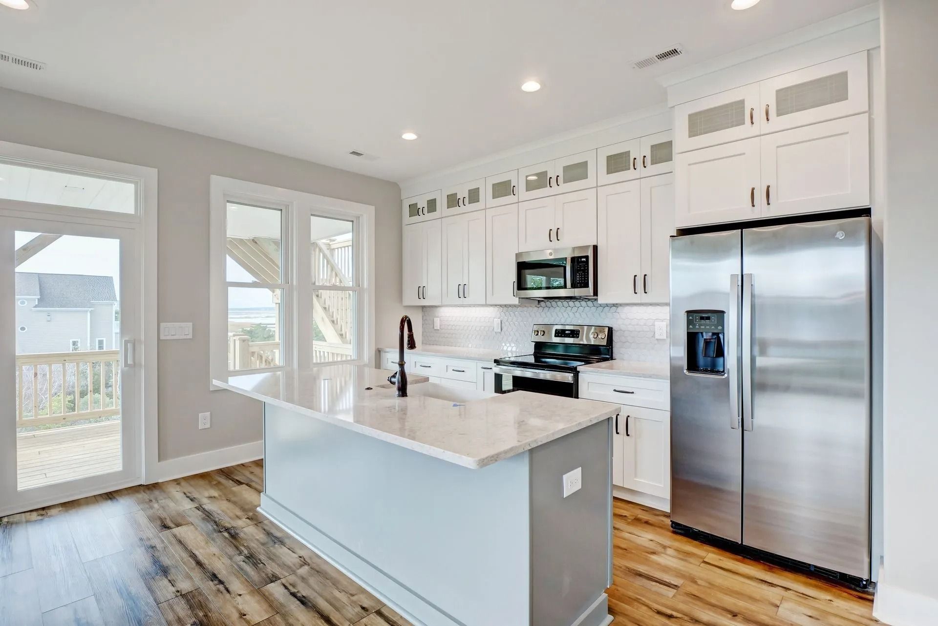 Modern white kitchen with island, stainless steel appliances, and wooden floors.