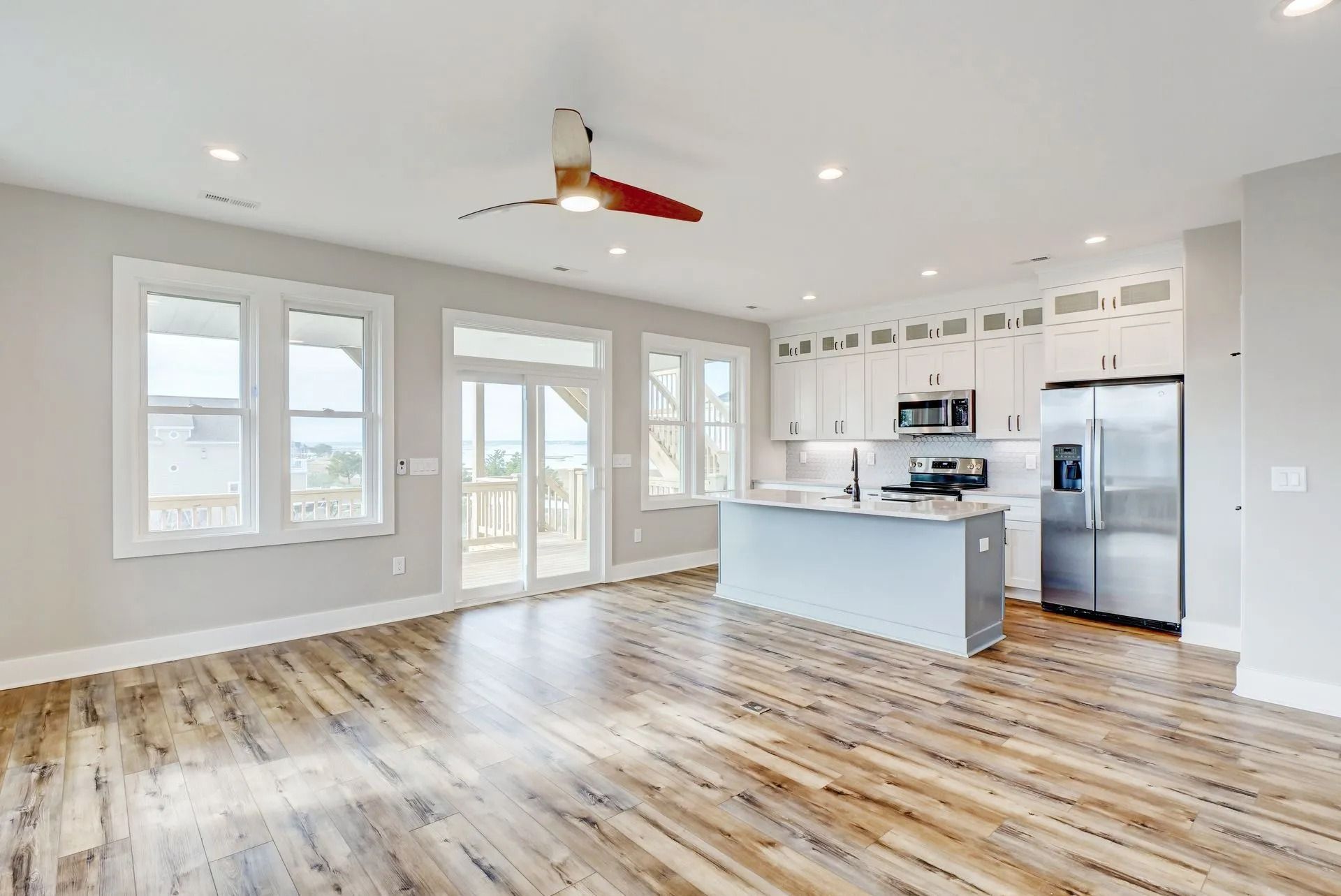 Open-concept kitchen and living area with wood floors, white cabinets, and a kitchen island. Sunlight streams in.