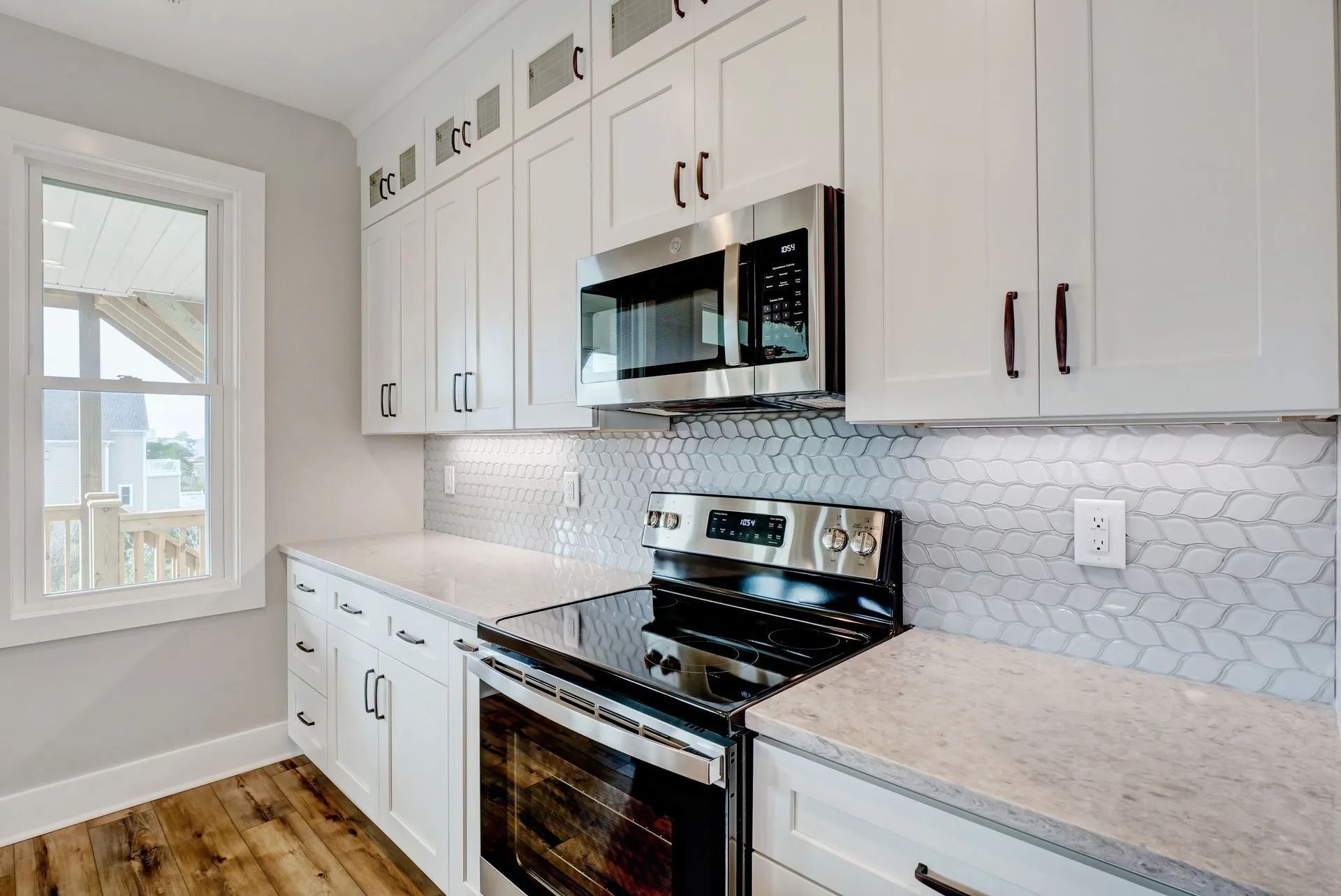 White kitchen with stainless steel appliances, backsplash, and cabinets, next to a window.
