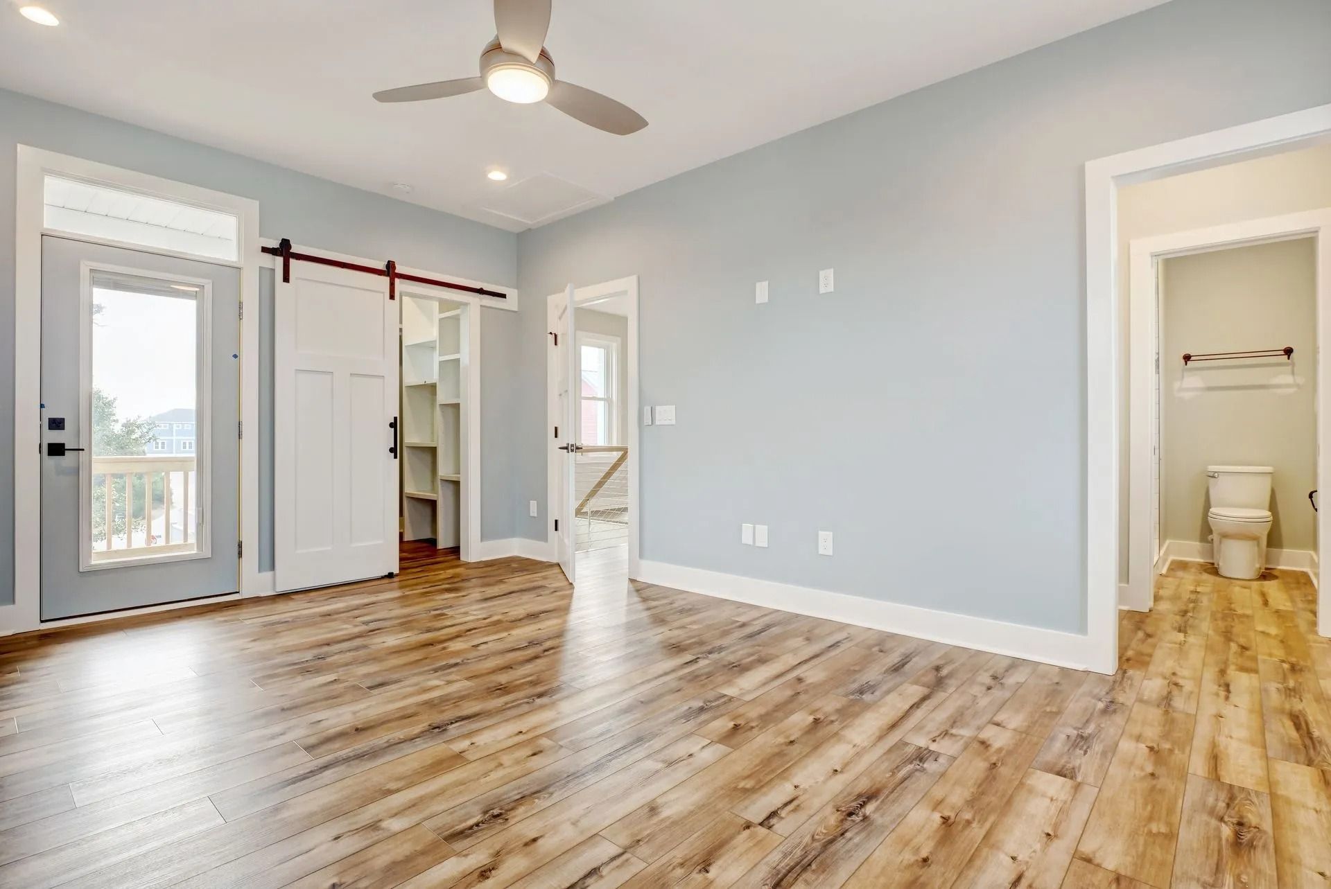 Bedroom with light blue walls, wooden floors, and a ceiling fan. Door to balcony and closet.