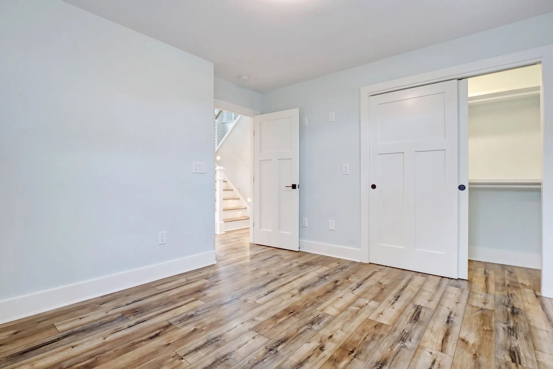 Empty bedroom with light blue walls, wood-look flooring, and white closet doors.