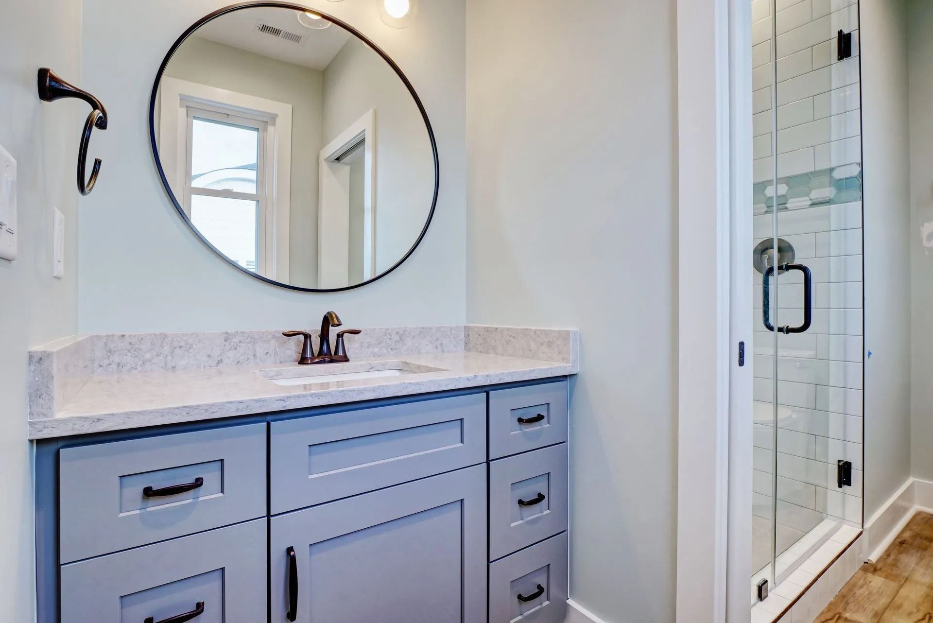 Bathroom with gray vanity, round mirror, and glass shower door.