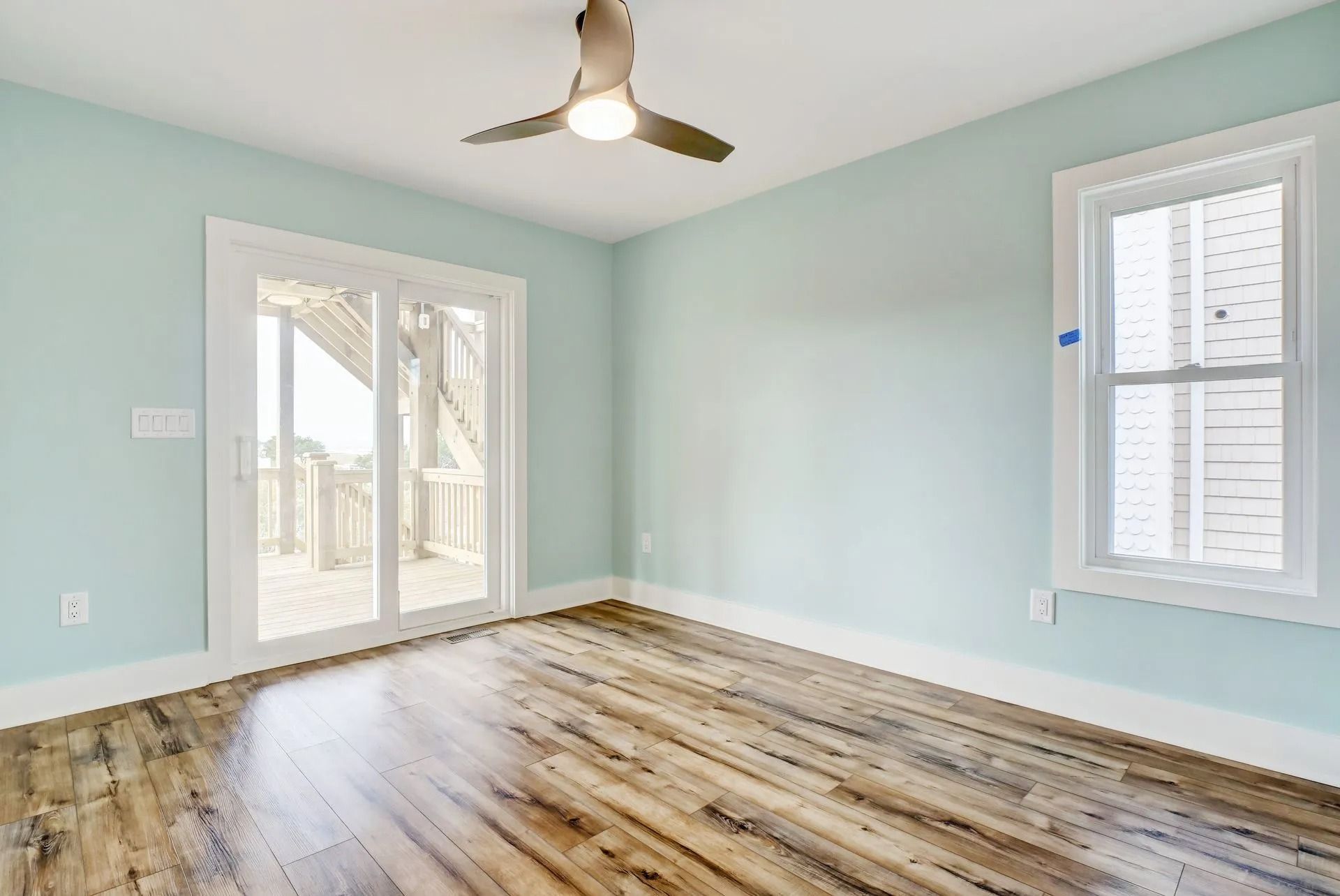 Empty room with blue walls, wood floor, sliding glass door to deck, and window with white trim.