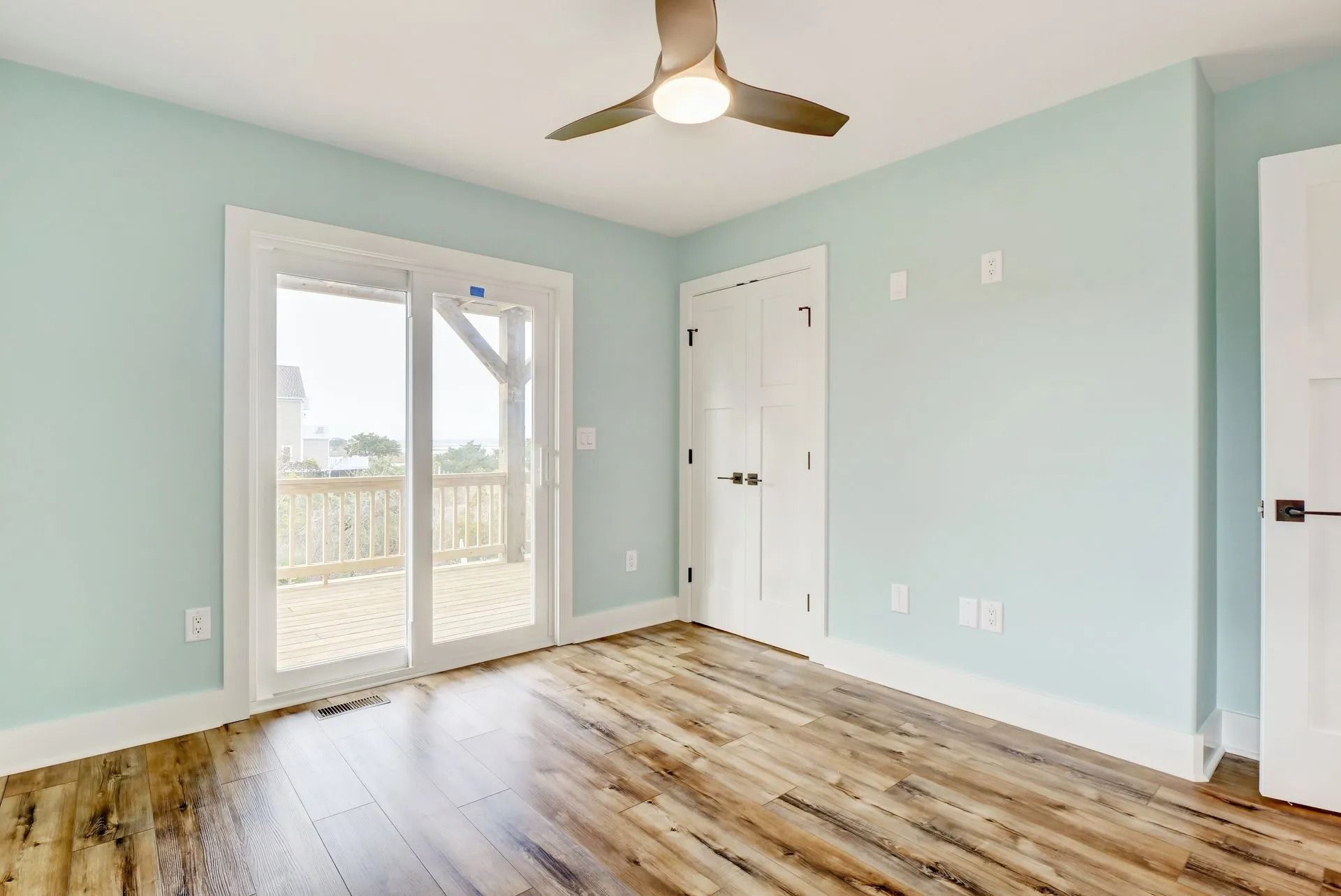 Bedroom with blue walls, sliding glass door to deck, wood-look floor, white trim, and ceiling fan.