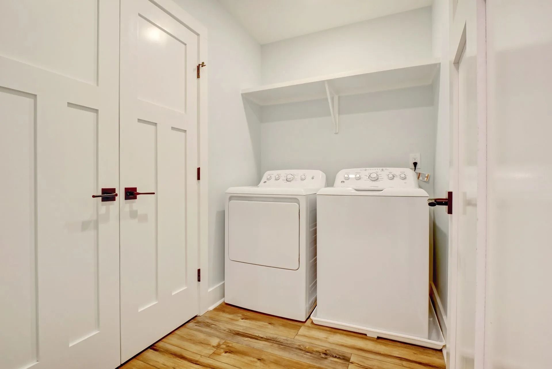 A laundry room with white washer and dryer, shelf, and white paneled doors.