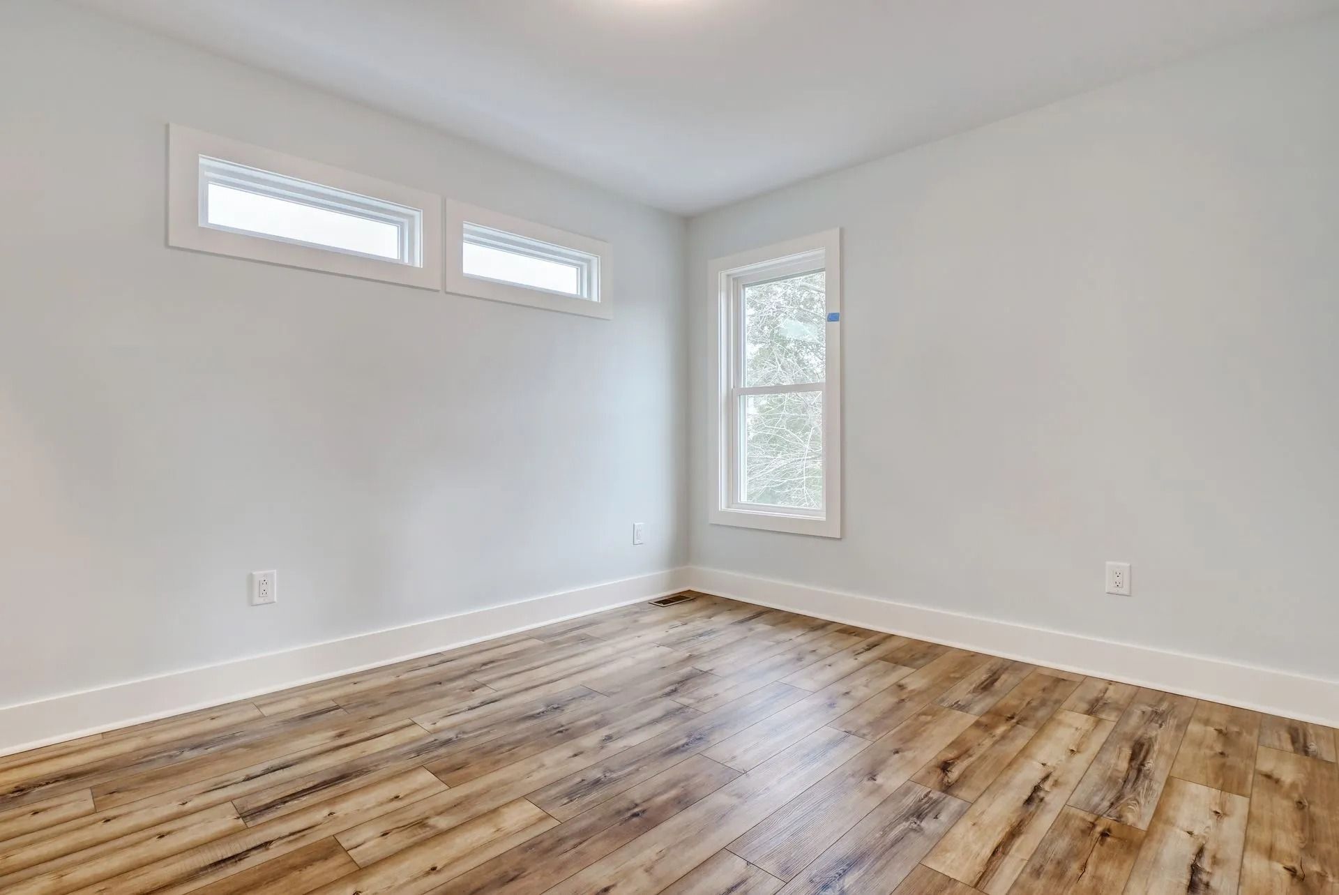 Empty room with wood floors and white walls, two windows at top, one tall window.
